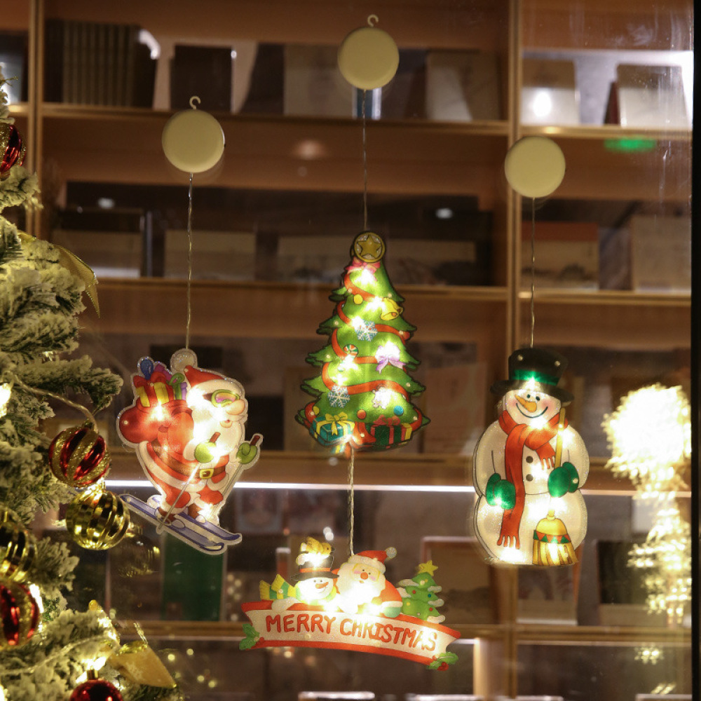 Fensterdekorationen zeigen einen Skifahrer-Weihnachtsmann, einen Weihnachtsbaum und einen Schneemann. Das Schild sagt Frohe Weihnachten. Links ist ein Weihnachtsbaum.