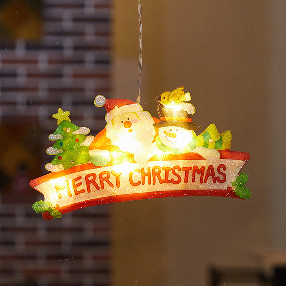 Eine leuchtende Weihnachtsdekoration mit Weihnachtsmann, Schneemann, Baum und Merry Christmas Banner. Es hängt vor einem Fenster.