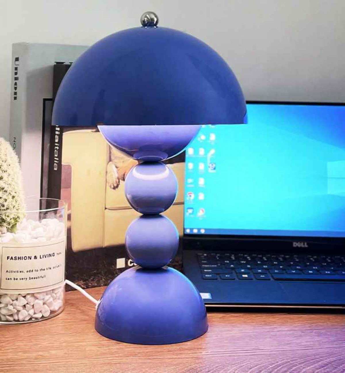Eine blaue Lampe mit drei Kugeln. Im Hintergrund ein Laptop, Bücher und eine Pflanze.