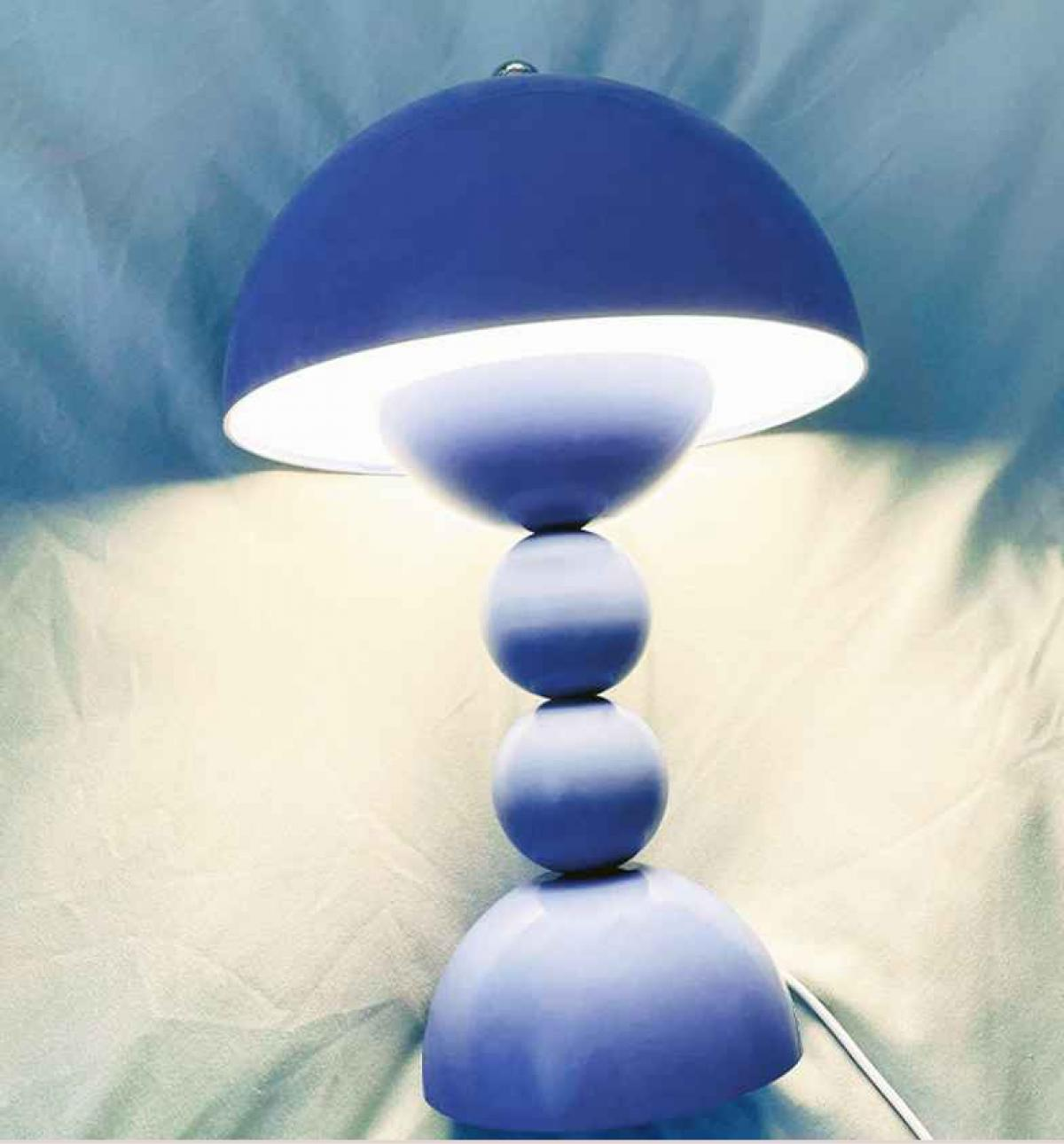 Eine blaue Lampe mit kuppelförmigem Schirm und kugelförmiger Basis steht auf weißem Untergrund. Die Lampe strahlt sanftes Licht aus.