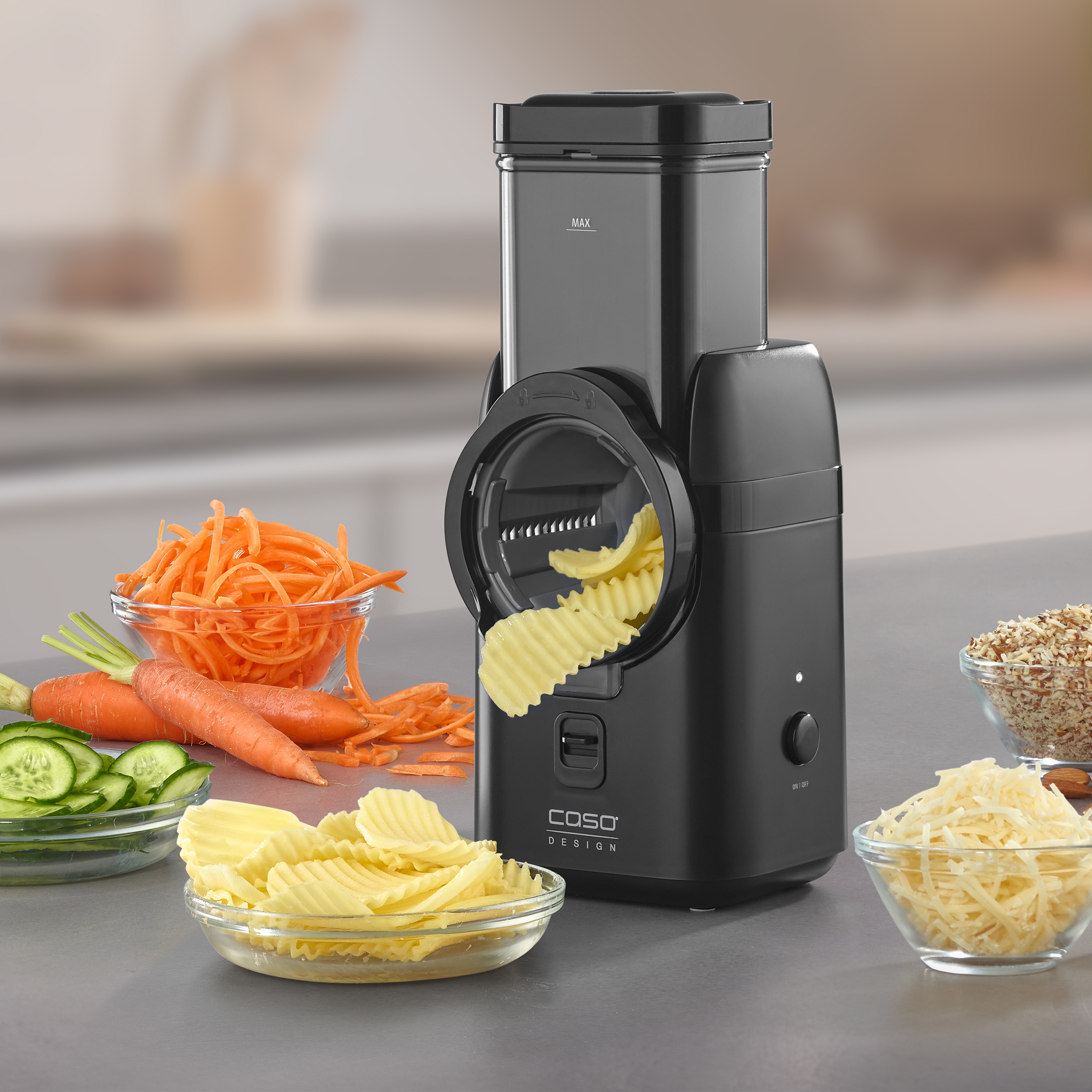 Un robot da cucina nero con verdure. Carote, cetrioli e formaggio sono in ciotole.