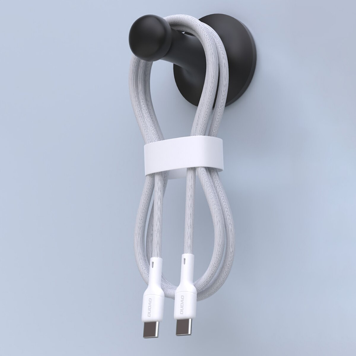 Ein graues USB-C-Kabel ist geschlungen und wird von einem weißen Band gehalten. Es hängt an einem schwarzen Haken an einer hellblauen Wand.