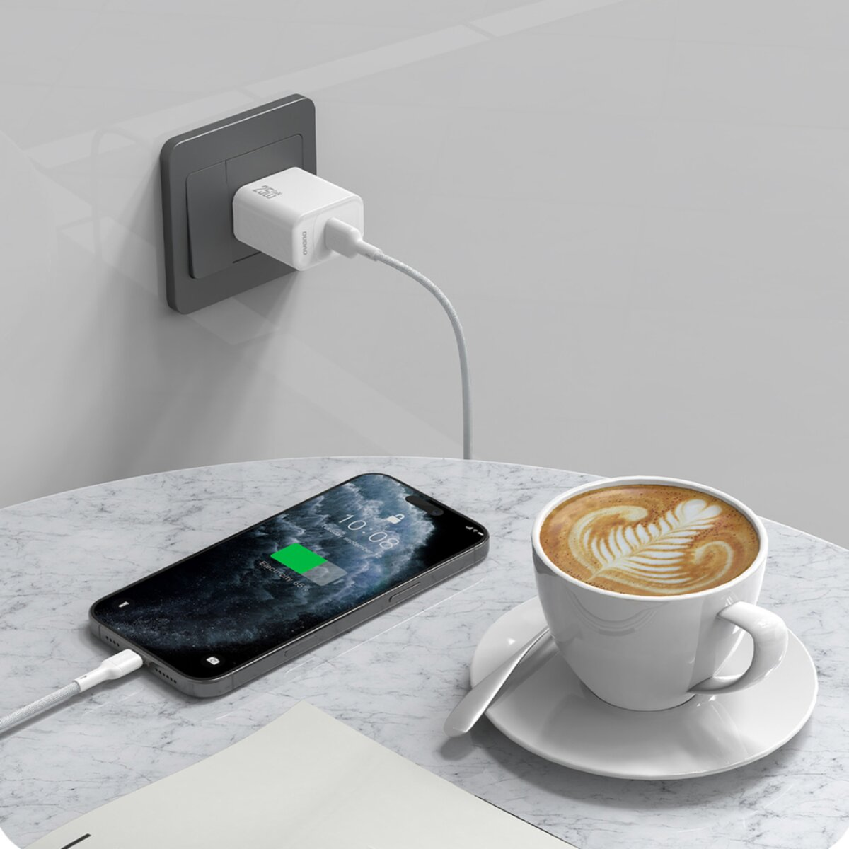 Ein Handy wird auf einem Marmortisch geladen. Eine Kaffeetasse, Ladegerät in der Wand. Das Handy zeigt 10:08 und 65% geladen.