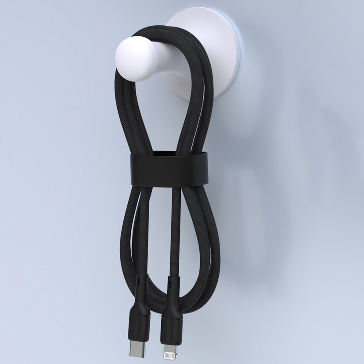 Schwarzes Ladekabel hängt an einem weißen Haken, der an einer hellblauen Wand befestigt ist. Das Kabel wird von einem schwarzen Riemen gehalten.