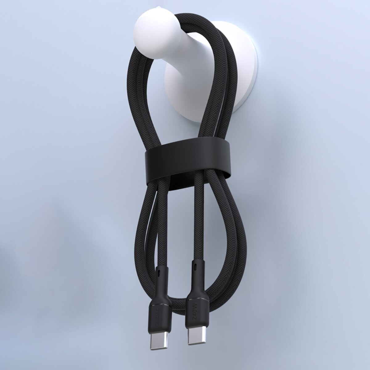 Ein schwarzes Ladekabel hängt an einem weißen Haken an einer hellblauen Wand. Das Kabel ist geschlungen und mit einem schwarzen Band befestigt.
