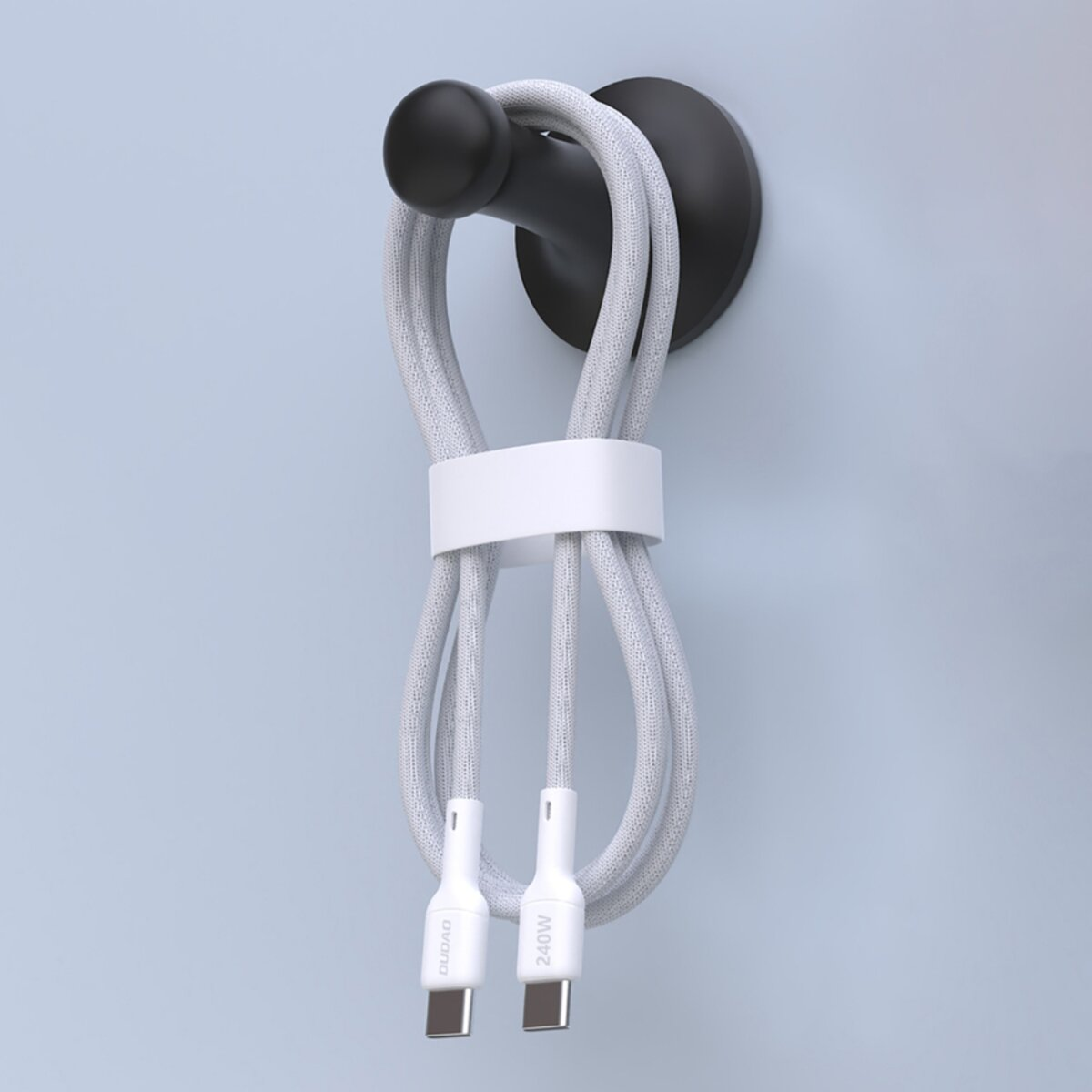 Ein graues USB-C-Kabel hängt an einem schwarzen Haken. Das Kabel wird von einem weißen Band gehalten. Der Hintergrund ist eine hellblaue Wand.