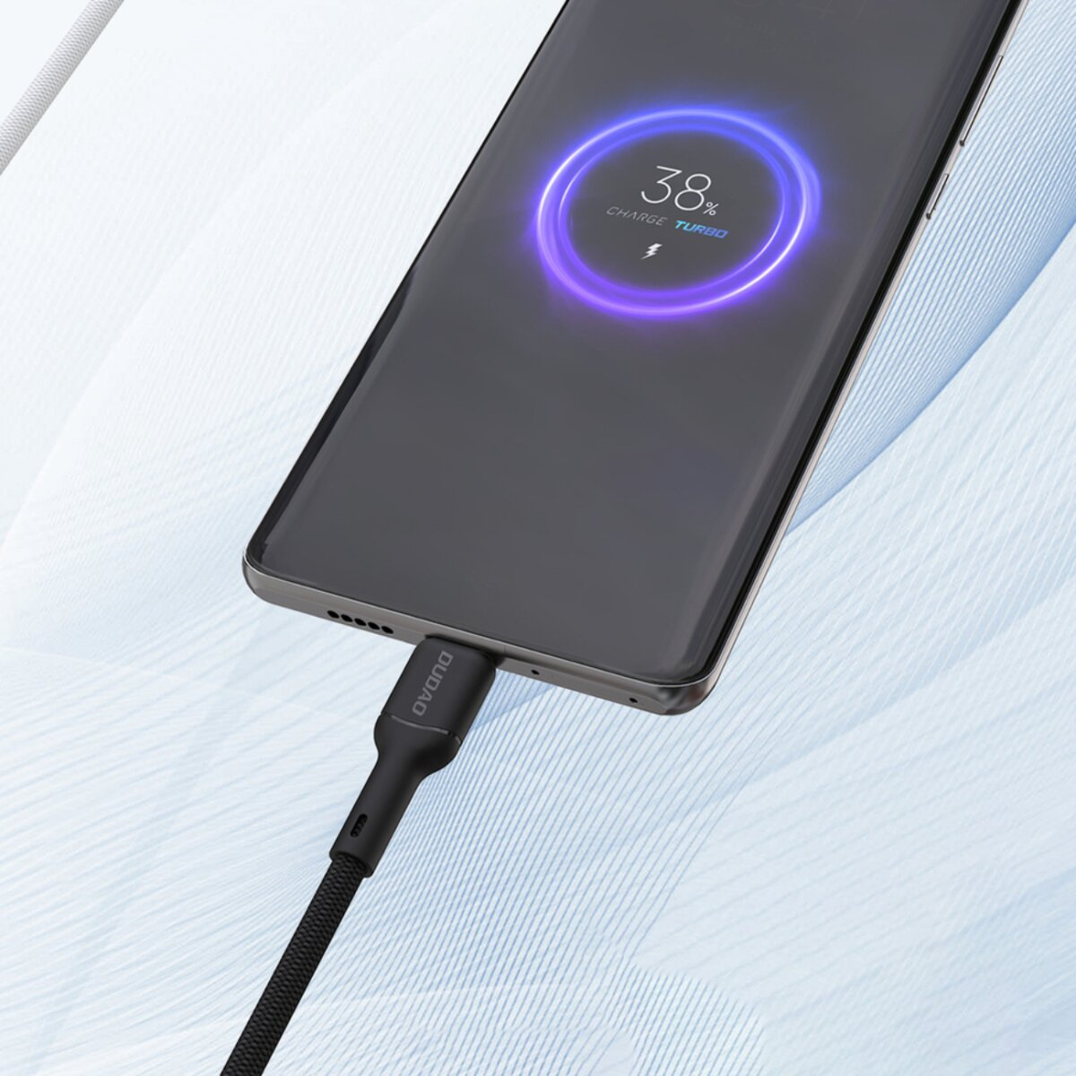 Ein schwarzes Smartphone lädt und zeigt 38% Akku an. Ein schwarzes Kabel ist angeschlossen. Der Hintergrund ist ein weiß-blauer Stoff.