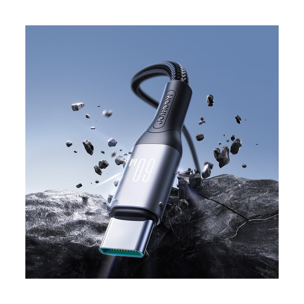 Nahaufnahme eines USB-C-Kabels mit der Aufschrift „JOYROOM“. Das Kabel ist silber und schwarz, mit einer Digitalanzeige „09“. Felsen im Hintergrund.