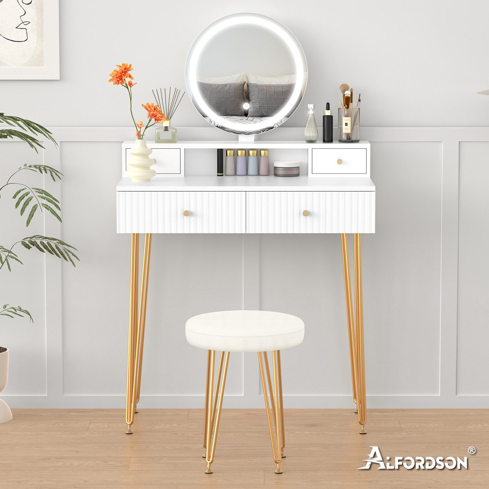 Ein weißer Schminktisch mit goldenen Beinen, Spiegel und Hocker. Auch orangefarbene Blumen, Schönheitsprodukte und eine Pflanze sind vorhanden.