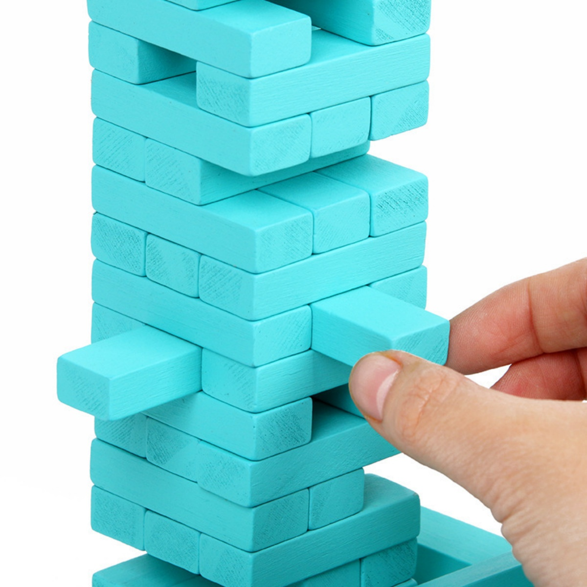 Eine Hand zieht einen türkisfarbenen Holzblock aus einem Turm aus ähnlichen Blöcken. Das Spiel ist auf weißem Grund.