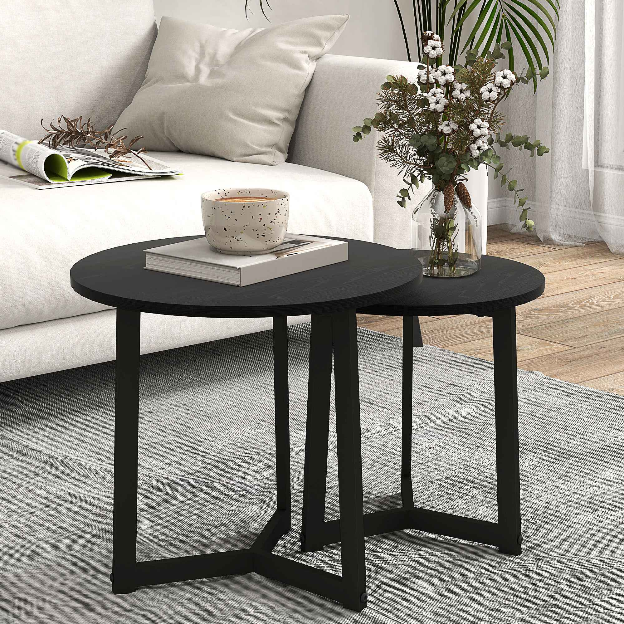 Zwei schwarze, runde Tische auf einem grauen Teppich. Ein weißes Sofa, eine Kaffeetasse und Blumen in einer Vase stehen auf den Tischen.