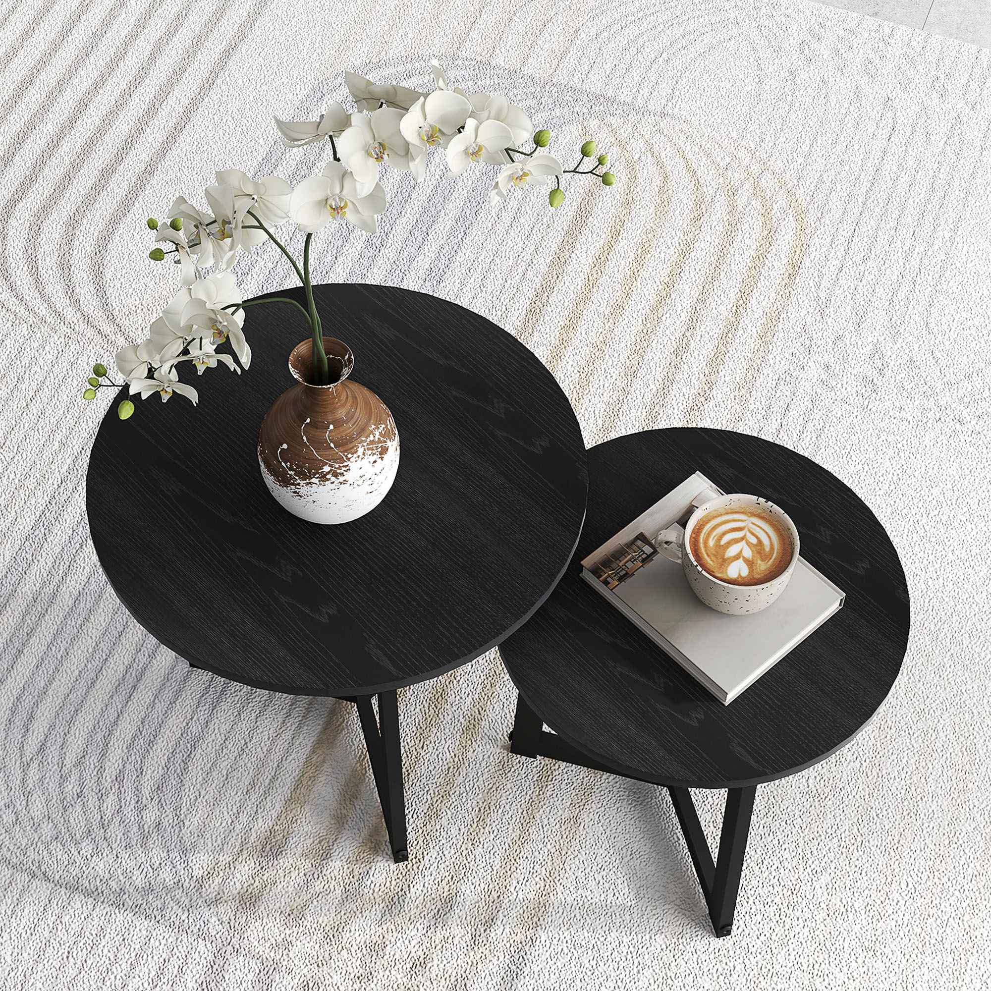 Zwei schwarze runde Tische mit einer Vase mit weißen Blumen und einer Kaffeetasse auf einem weißen Teppich.
