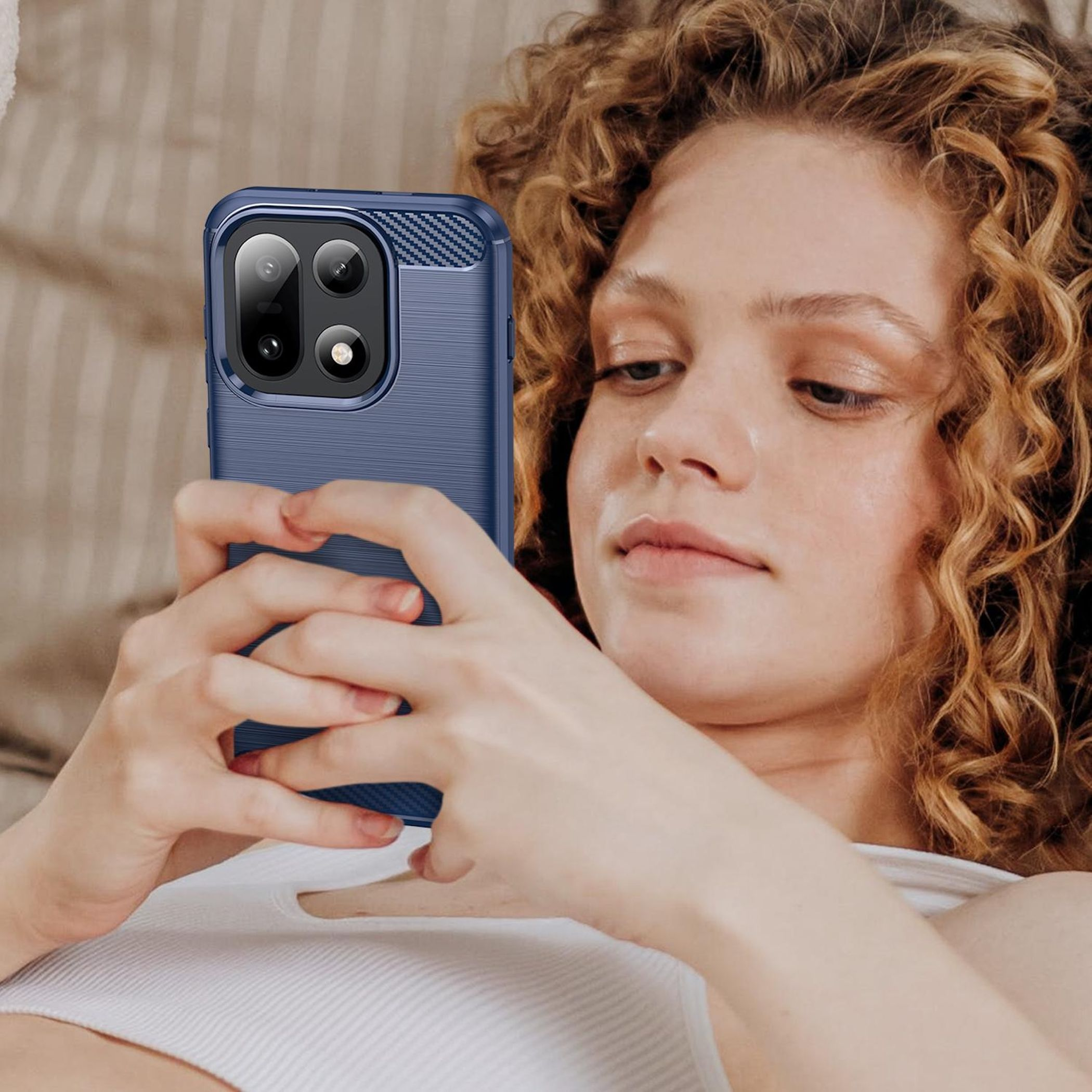 Eine Frau mit lockigem Haar hält ein blaues Telefon. Sie schaut mit neutralem Gesichtsausdruck auf das Telefon.