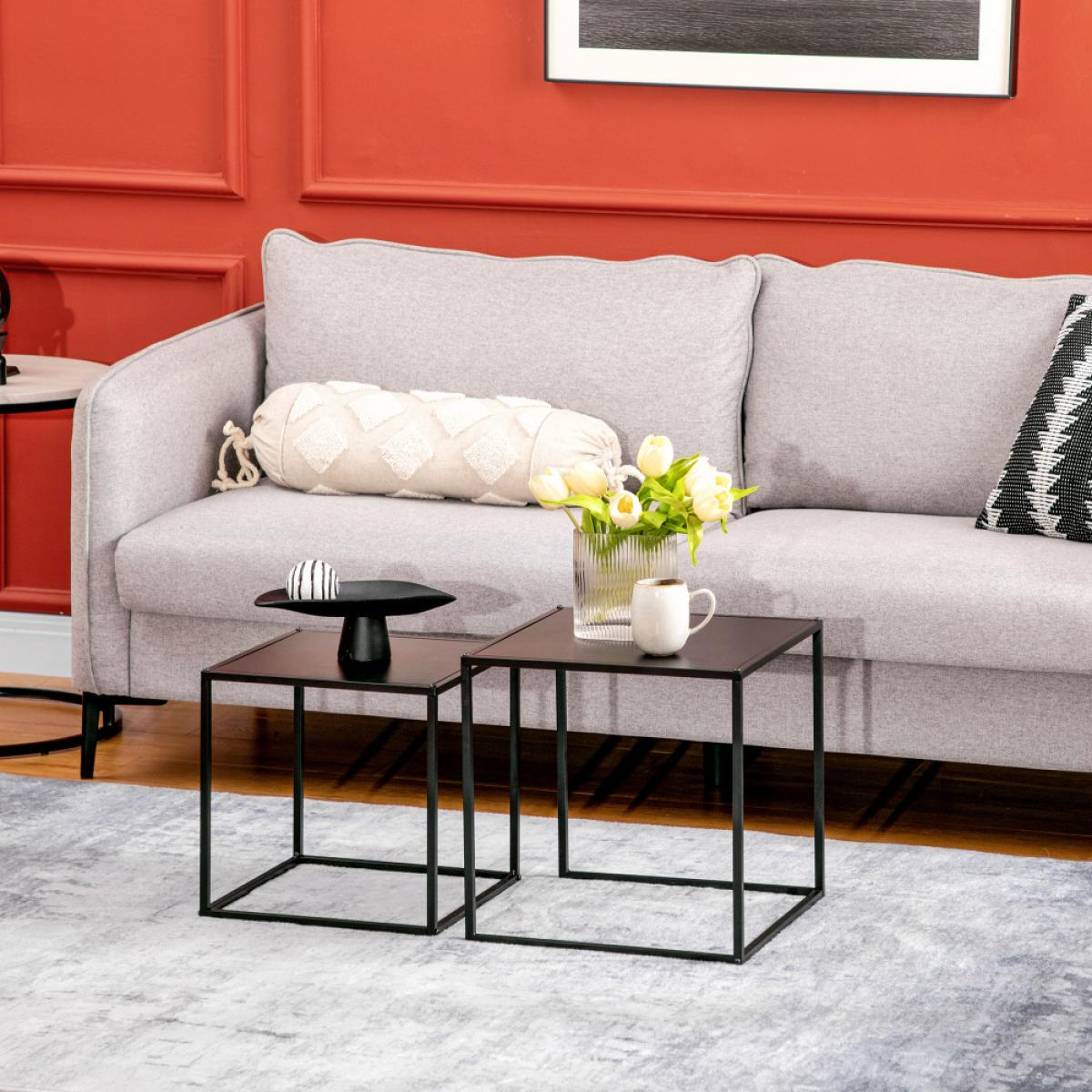 Wohnzimmerszene mit grauem Sofa, zwei schwarzen Tischen und roter Wand. Blumen und eine Tasse stehen auf einem Tisch.