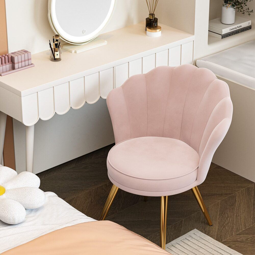 Ein rosa muschelförmiger Stuhl mit goldenen Beinen steht in der Nähe eines Schminktisches mit Spiegel. Ein Bett mit Gänseblümchen-Kissen im Vordergrund.