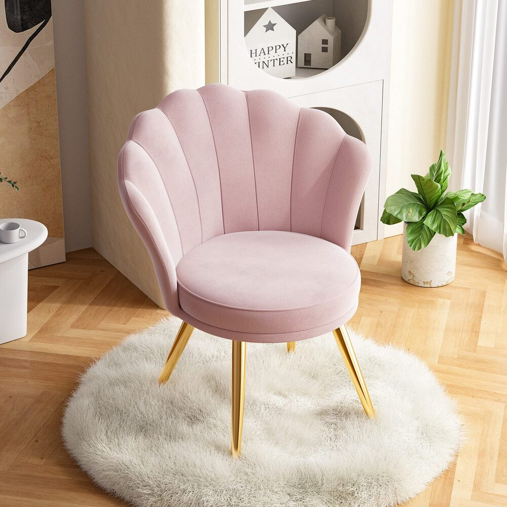Ein rosa Samtstuhl mit goldenen Beinen steht auf einem weißen, flauschigen Teppich. Im Hintergrund sind eine Topfpflanze und ein dekoratives Regal zu sehen.
