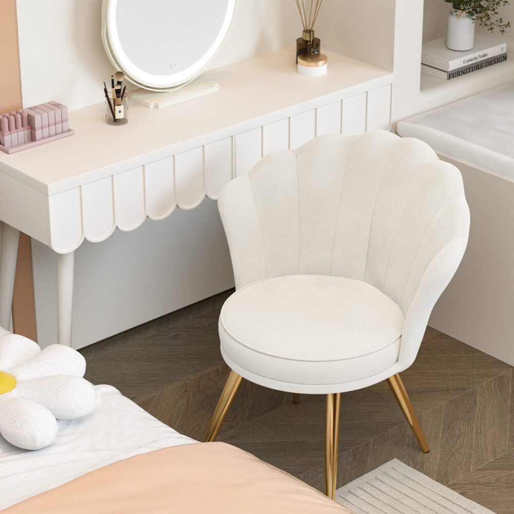 Ein weißer Schminktisch mit Spiegel, ein muschelförmiger Stuhl und ein Blumenkissen auf einem Bett. Der Stuhl hat goldene Beine. Der Raum hat Holzböden.