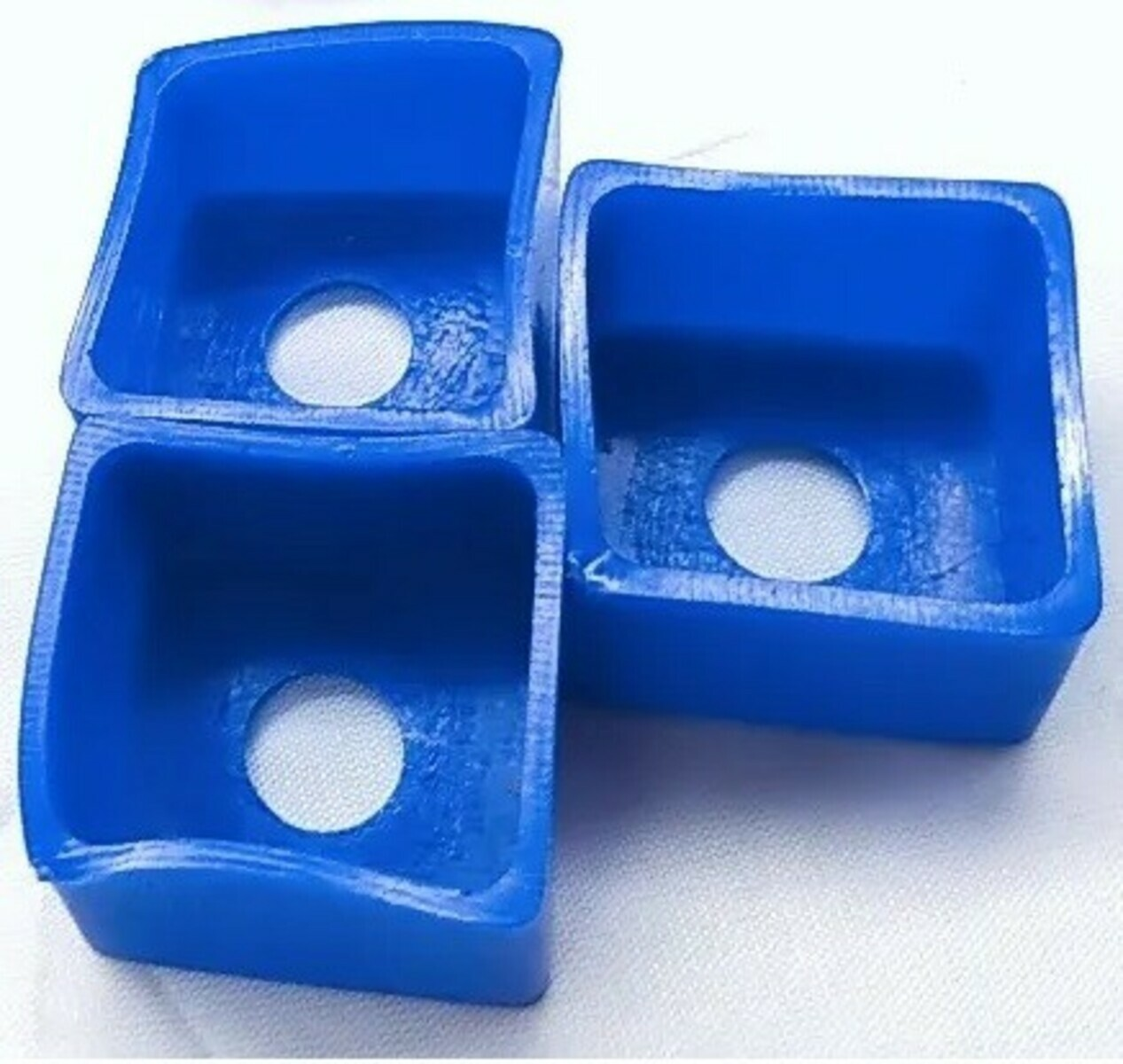 Drie blauwe, vierkante containers zijn op elkaar gestapeld. Elk heeft een ronde, witte opening aan de onderkant. De achtergrond is wit.