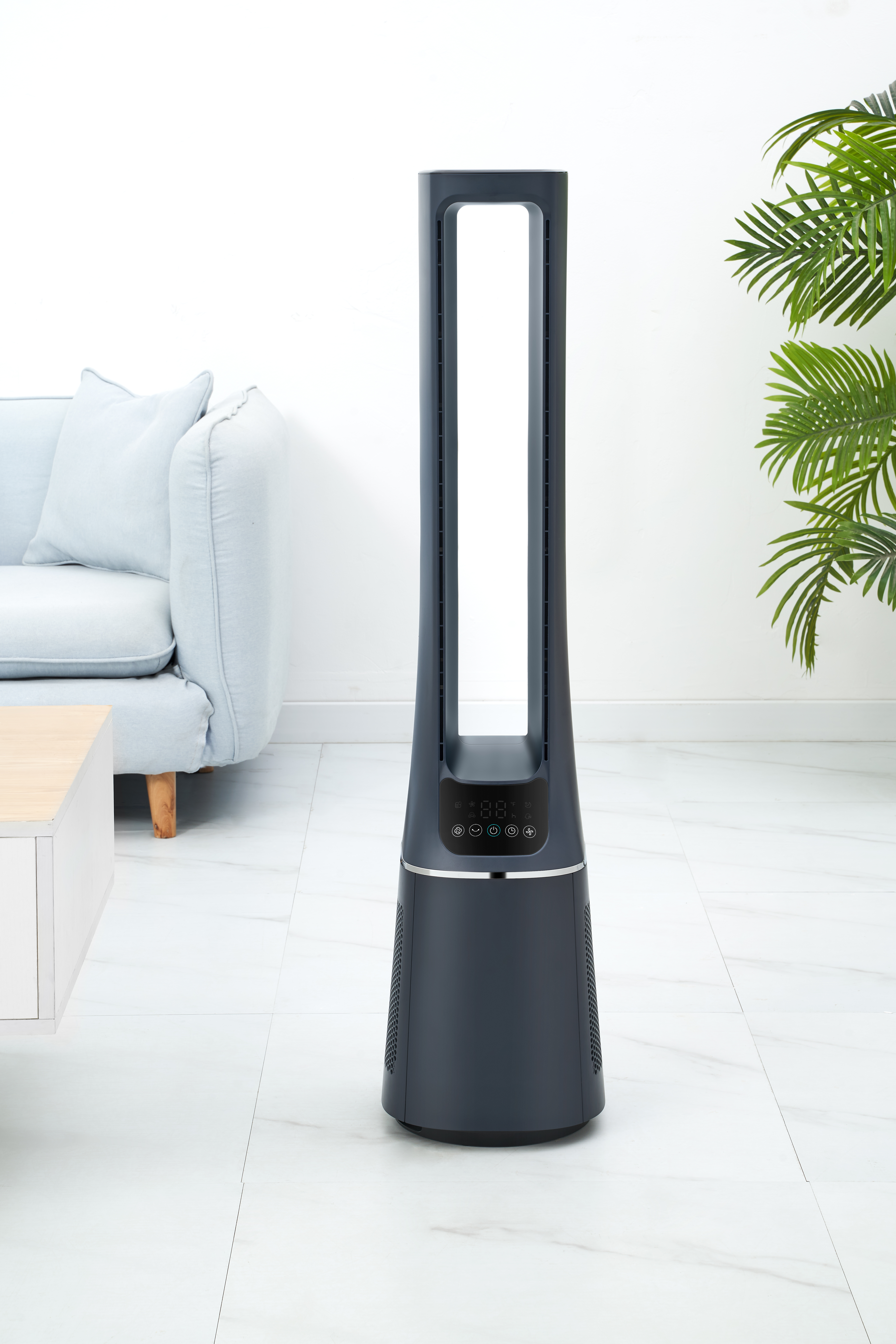 Dunkelgrauer Turmventilator steht auf weißem Fliesenboden. Hellblaues Sofa und grüne Pflanze im Hintergrund.