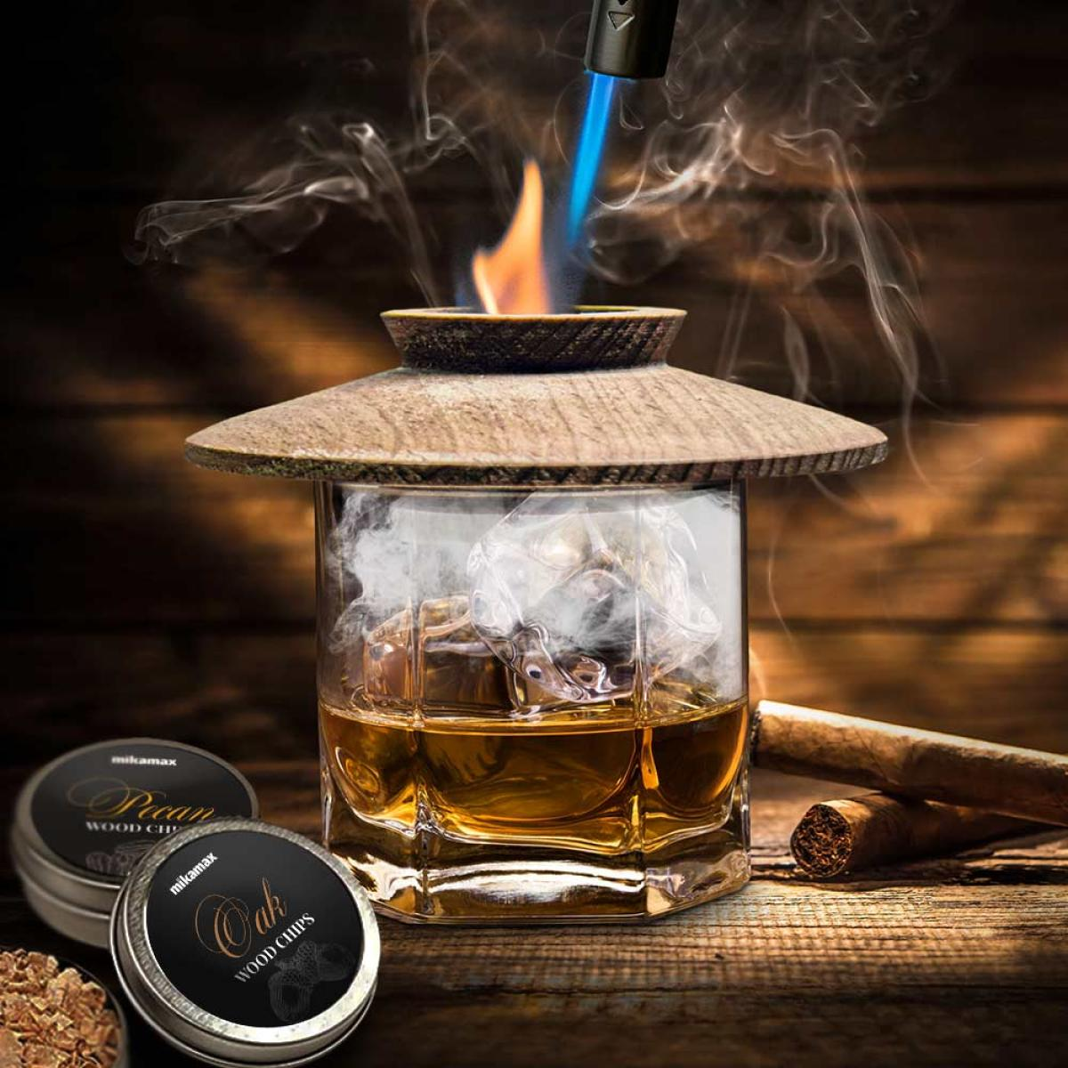 A glass with ice and whiskey, a wooden lid with fire, smoke, wood chips, and a cigar on a wooden surface.