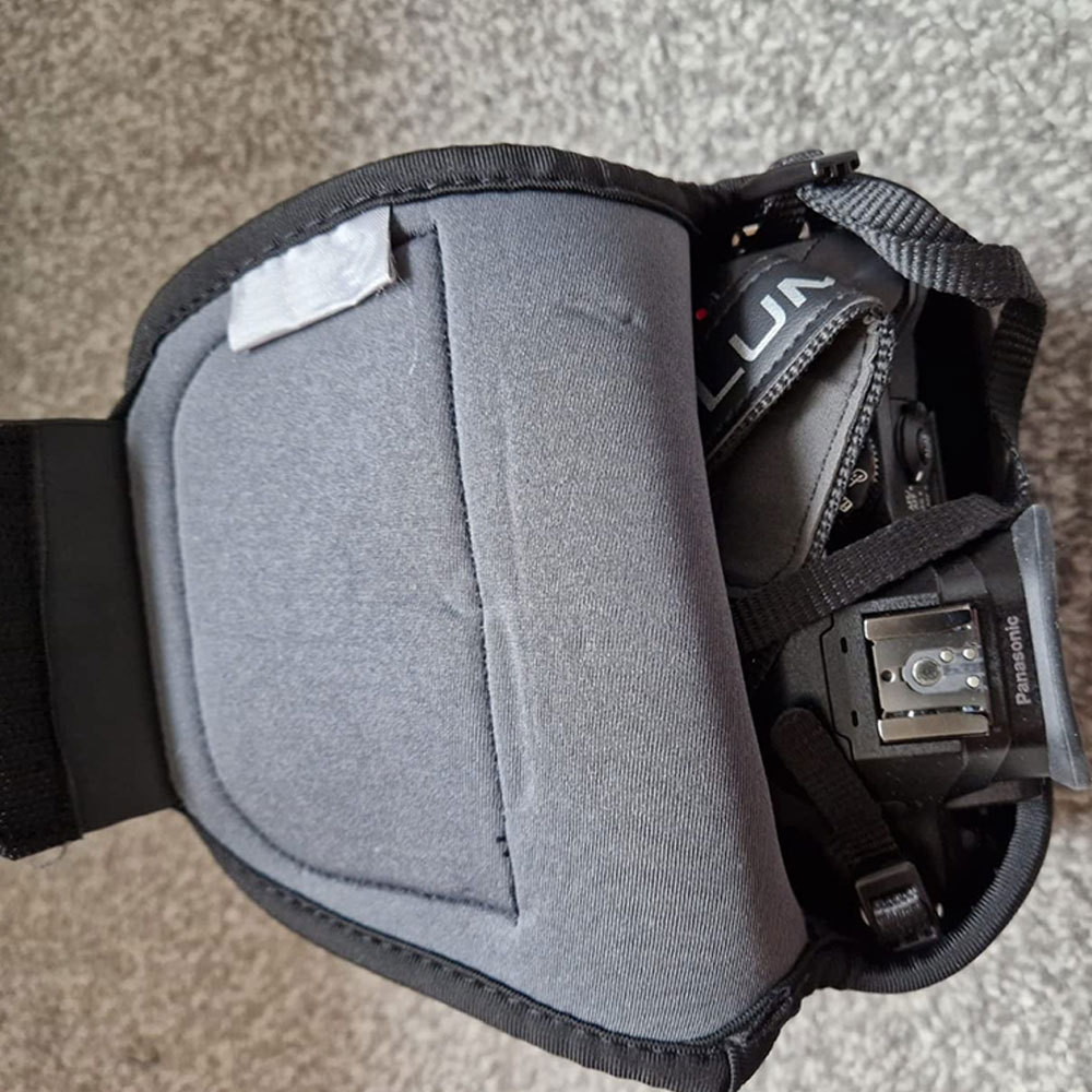 Eine grau gepolsterte Kameratasche, die teilweise geöffnet ist und eine schwarze Kamera mit sichtbarem 'LUMIX' zeigt. Die Tasche liegt auf einer grauen Oberfläche.