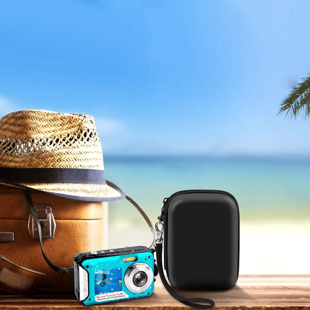 Reiseszene mit Koffer, Hut, Kamera und Etui auf einer Holzoberfläche vor Strandhintergrund.