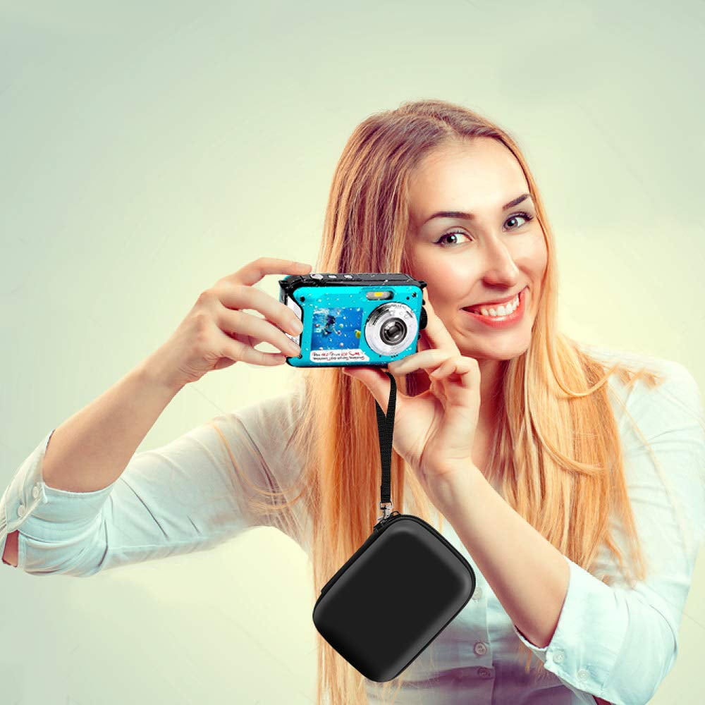 Eine Frau mit blonden Haaren hält eine blaue Kamera und lächelt. Eine schwarze Hülle hängt an der Kamera. Der Hintergrund ist weich grün.