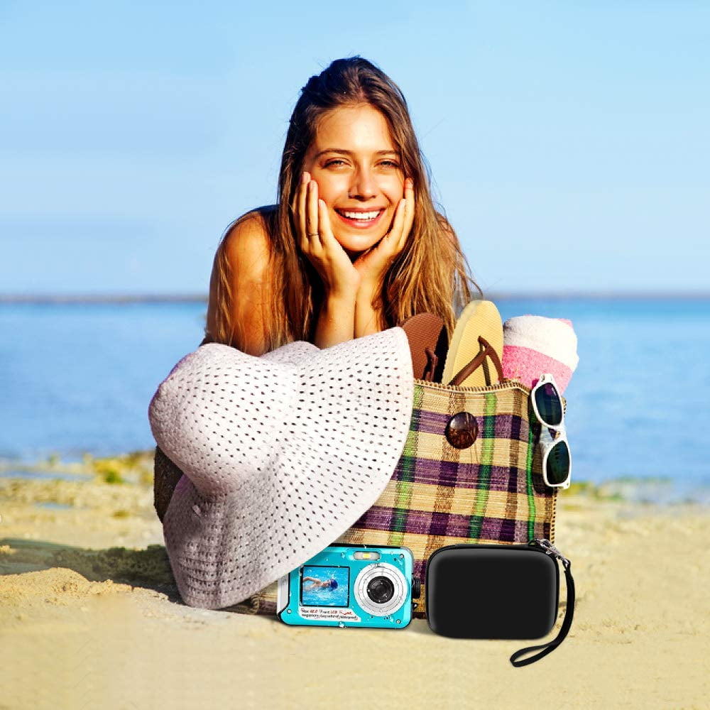 Eine Frau lächelt neben einer Strandtasche mit Strandutensilien. Vorne eine Kamera und ein schwarzes Etui. Blauer Himmel und Meer im Hintergrund.