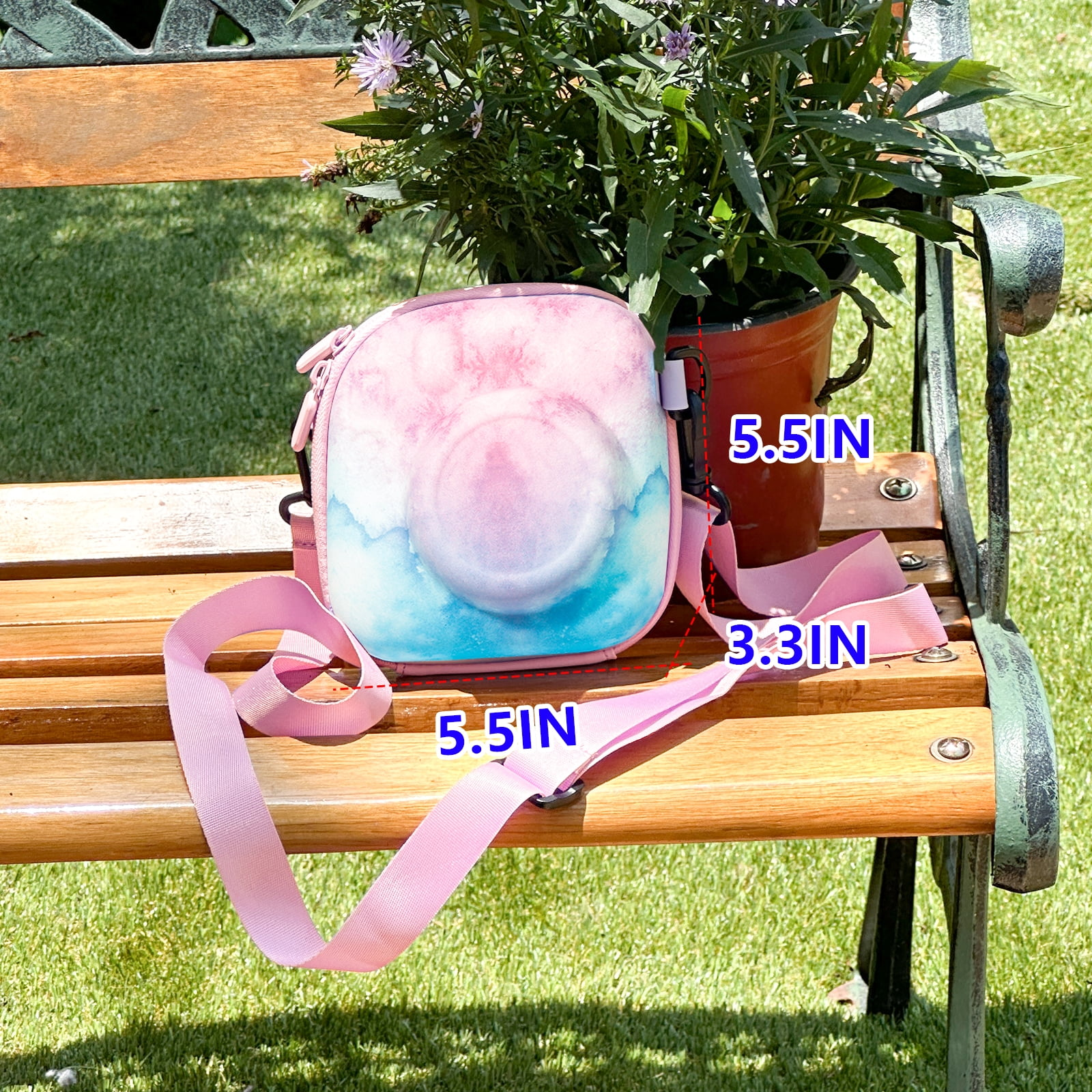 Eine rosa-blaue Kameratasche mit pinkfarbenem Riemen liegt auf einer Holzbank. Im Hintergrund steht eine Pflanze in einem braunen Topf.