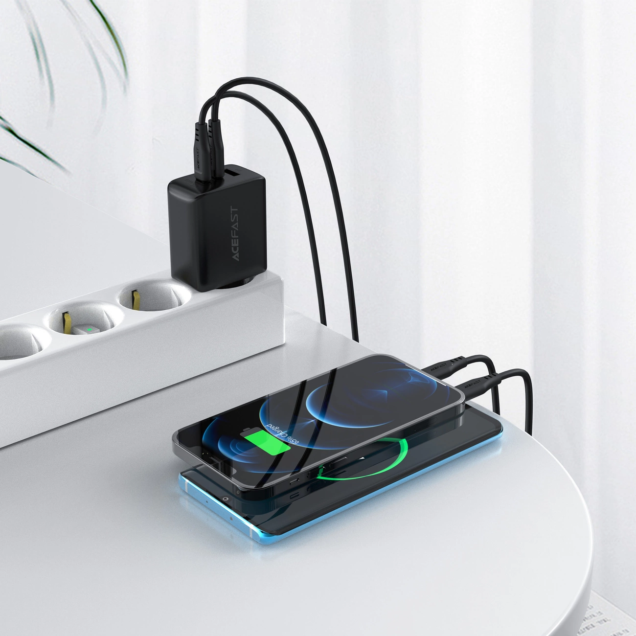 Zwei Smartphones laden auf einem weißen Tisch. Ein schwarzer Netzadapter ist an eine Steckdosenleiste angeschlossen. Die Telefone zeigen 65% geladen an.