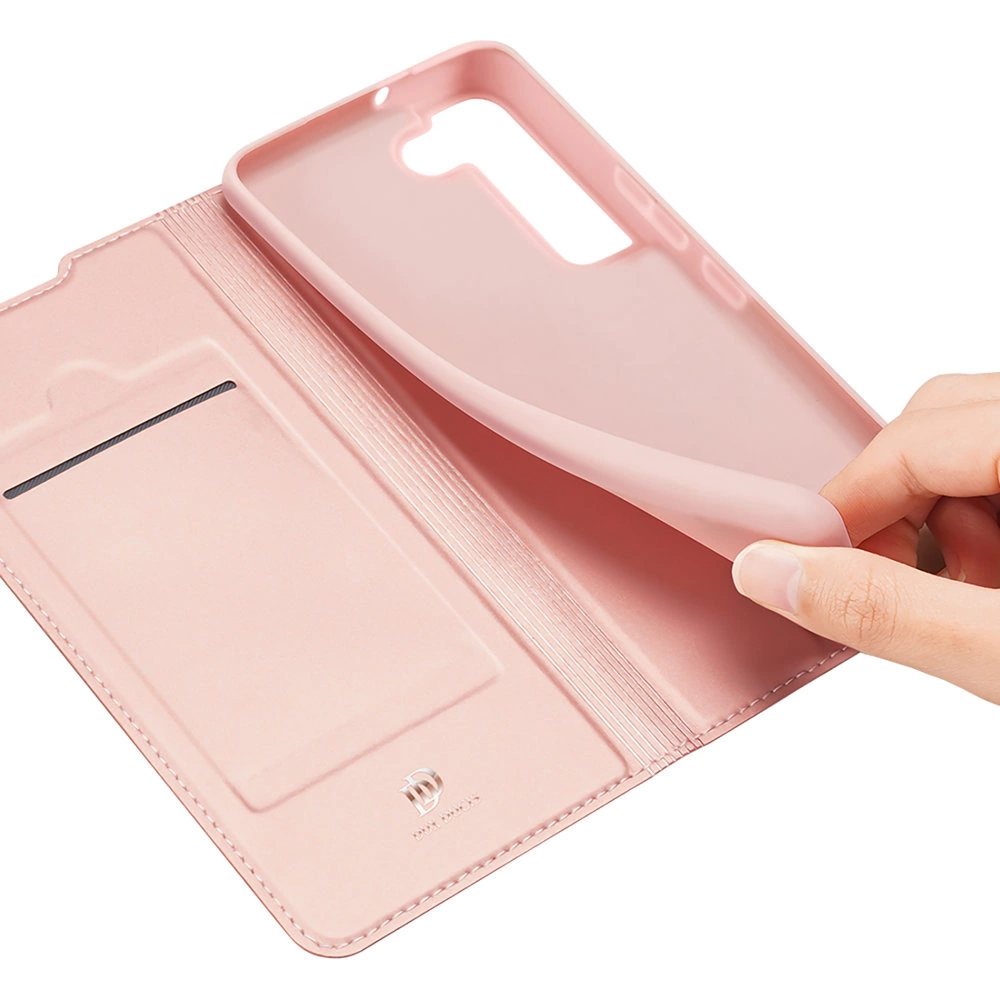 Una mano tiene aperta una custodia rosa. La custodia è simile alla pelle con uno slot per carte. Il supporto del telefono è anche rosa.
