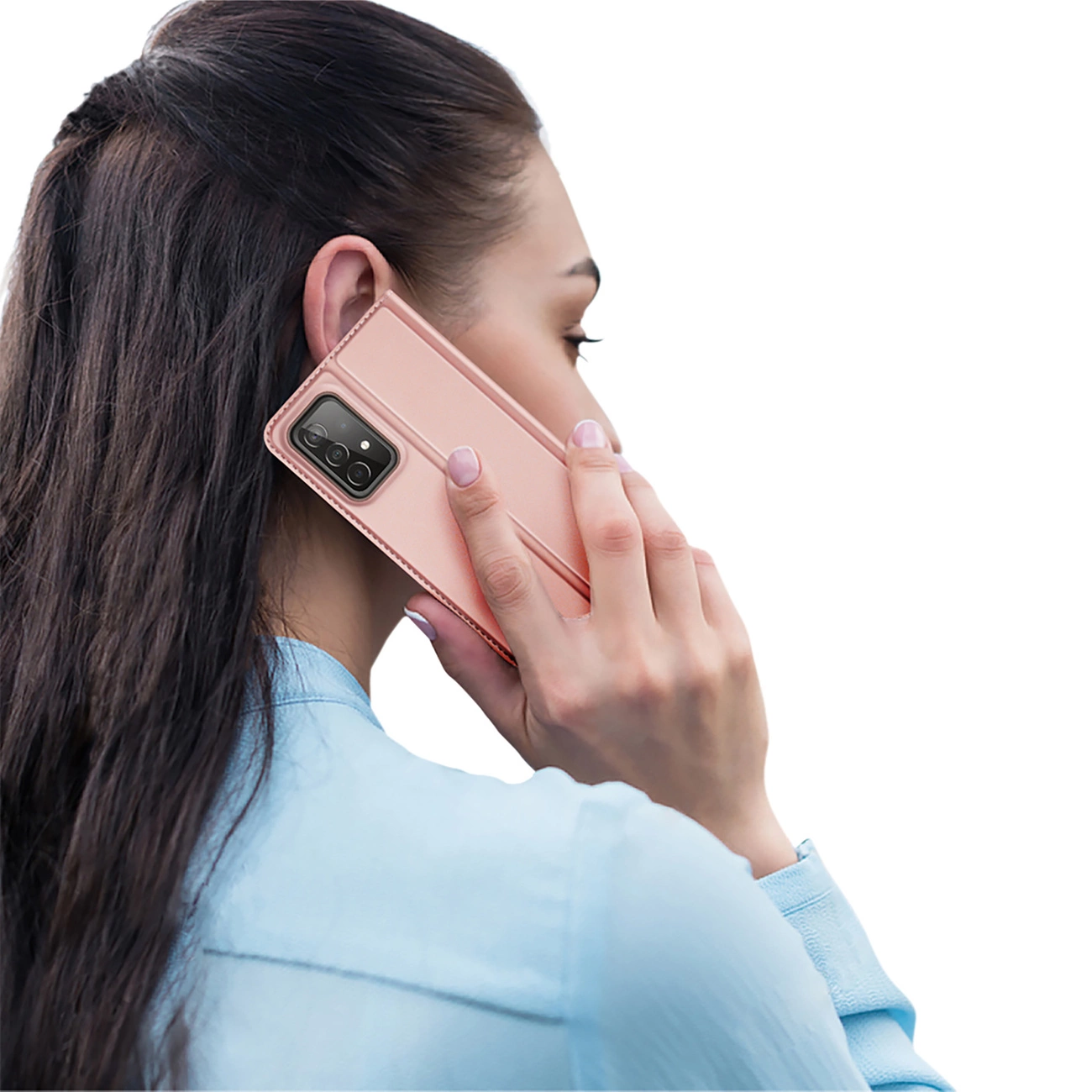 Una donna tiene un telefono color oro rosa all'orecchio. Indossa una camicia azzurra e ha i capelli scuri. Lo sfondo è bianco.