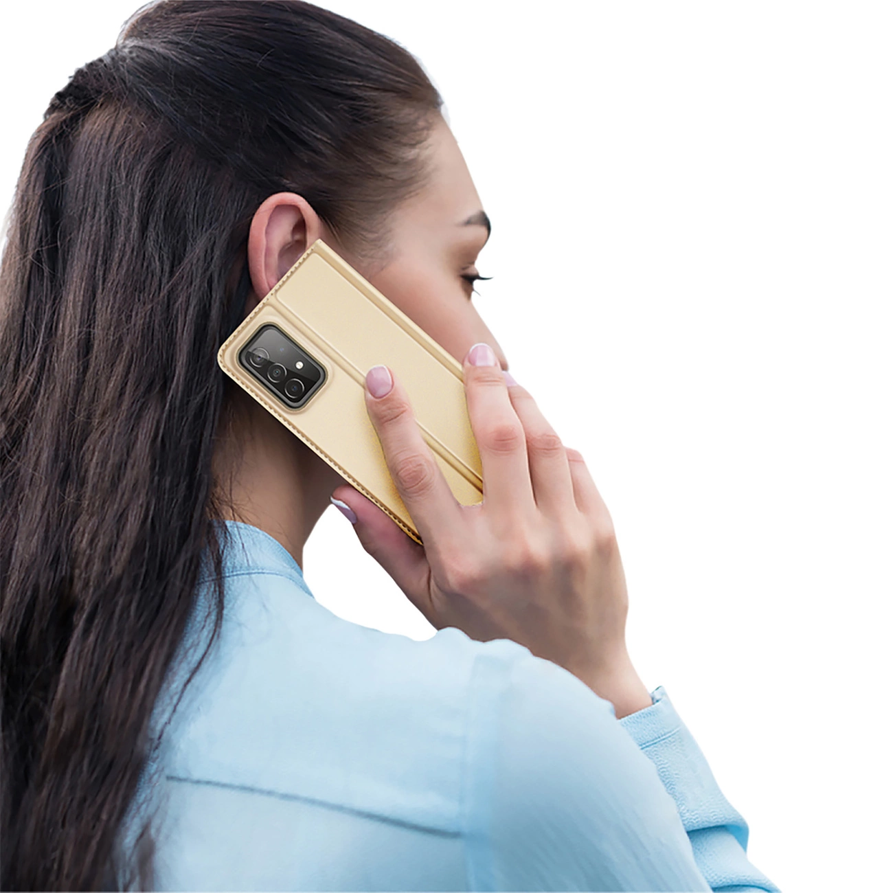Una donna tiene una custodia dorata del telefono all'orecchio. Indossa una camicia blu con i capelli scuri. Lo sfondo è bianco.