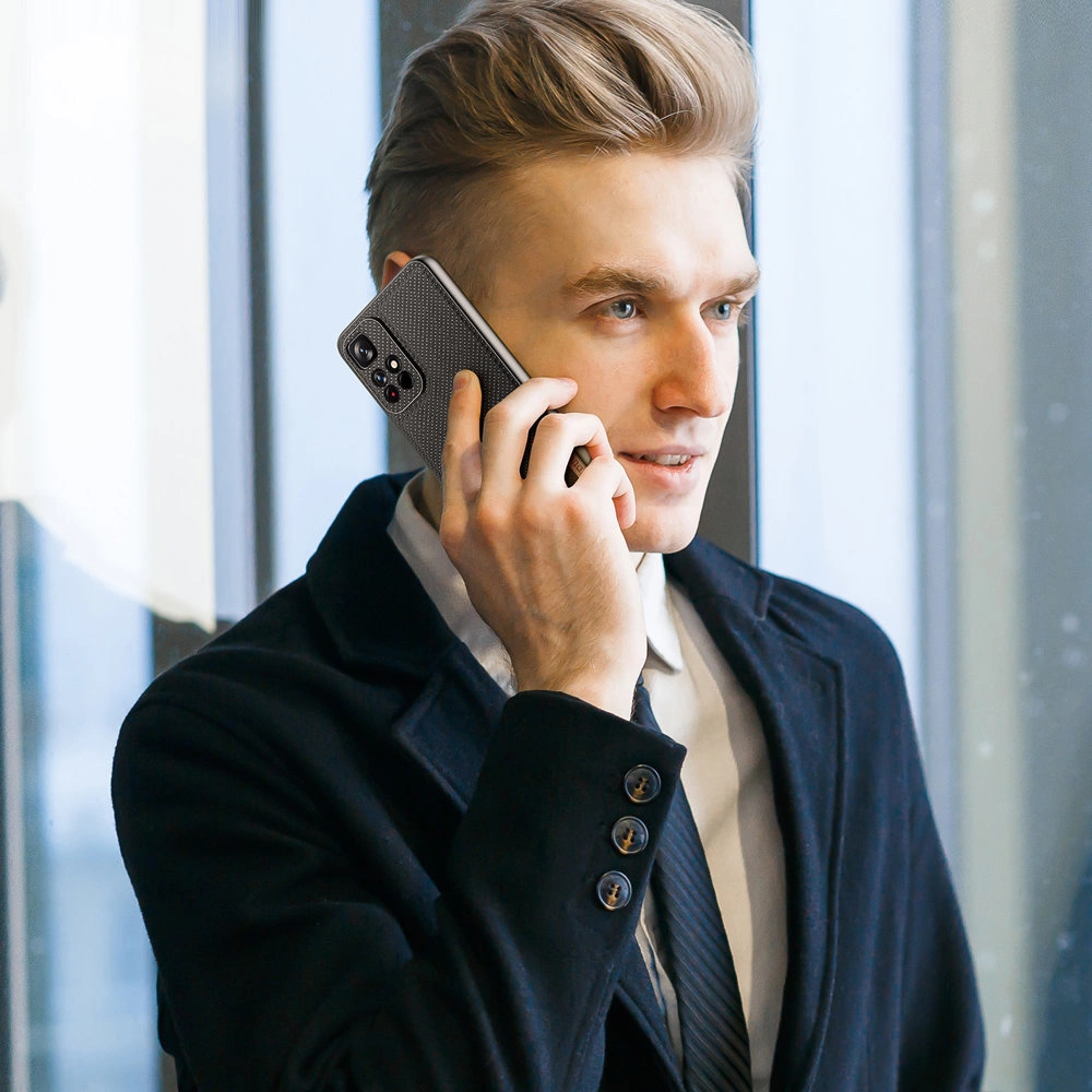Un uomo con un cappotto nero parla al telefono. Ha i capelli biondi e una cravatta. Lo sfondo è una finestra sfocata.