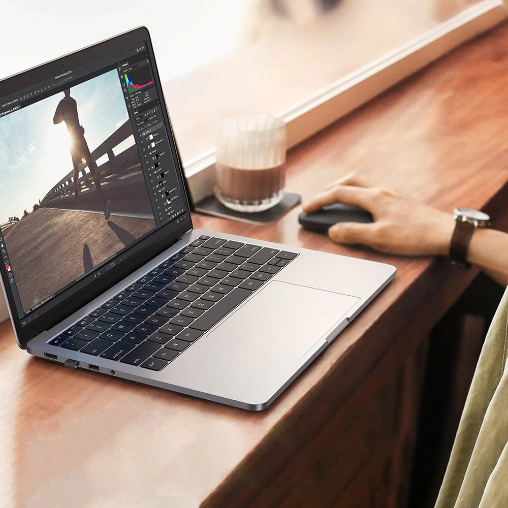 Laptop auf einem Holztisch. Eine Person benutzt eine Maus. Ein Glas Kaffee ist vorhanden. Der Laptop-Bildschirm zeigt ein Bild.