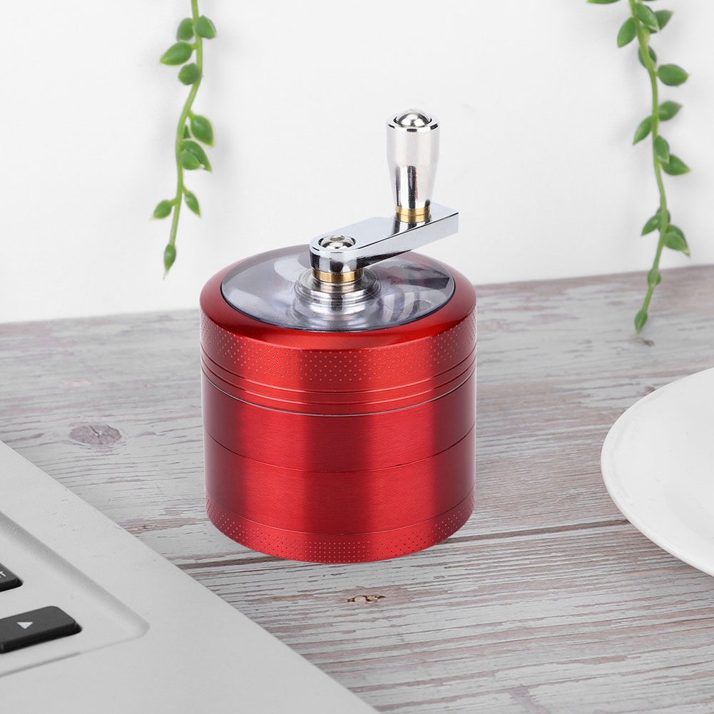 Ein roter Grinder mit silbernem Griff. Er steht auf einem Holztisch mit Laptop und weißem Teller. Grüne Pflanzen im Hintergrund.