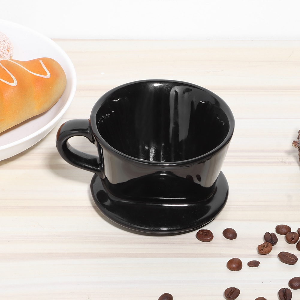 Eine schwarze Kaffeetasse auf einer Untertasse. Kaffeebohnen und Gebäck liegen daneben auf einer hellen Holzoberfläche.