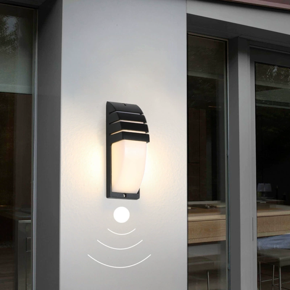 Eine schwarze Außenwandleuchte ist an einer weißen Wand montiert. Die Lampe hat darunter einen Bewegungssensor. Glastür rechts.