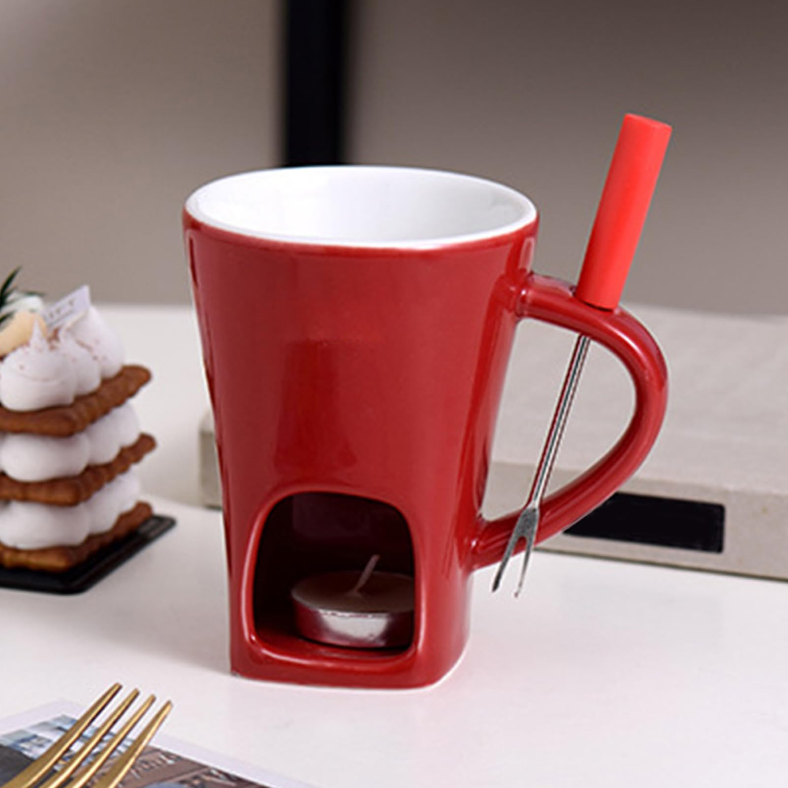 Eine rote Fondue-Tasse mit einer Kerze, einem Dessert und einer Gabel. Die Tasse hat einen Griff und eine rote Oberseite.