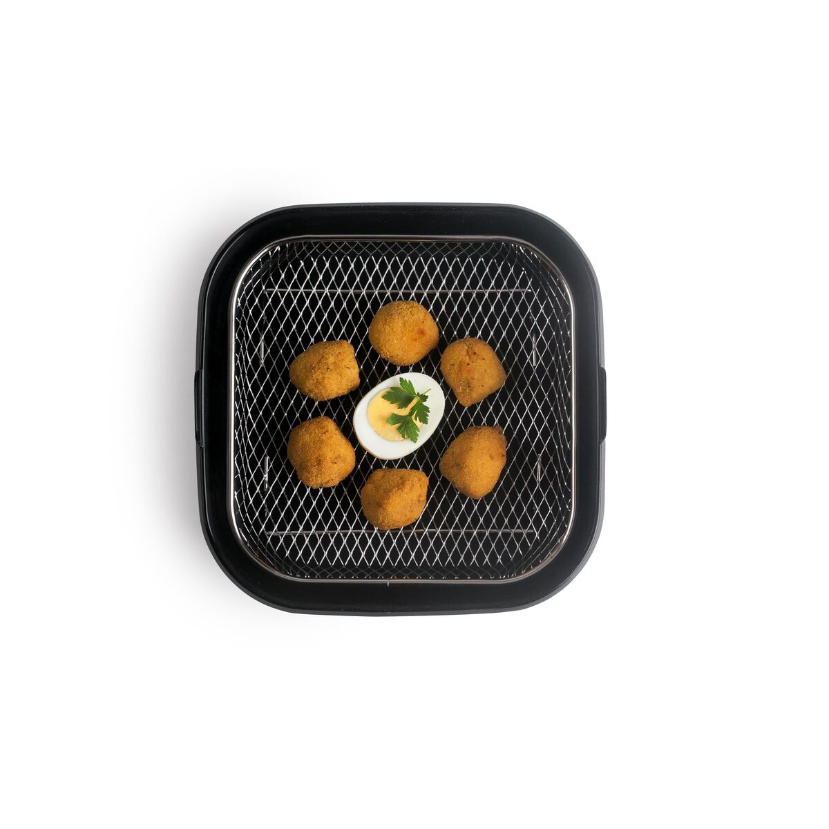 Draufsicht zeigt einen Airfryer-Korb mit frittierten Speisen und einem halbierten gekochten Ei mit Petersilie. Weißer Hintergrund.