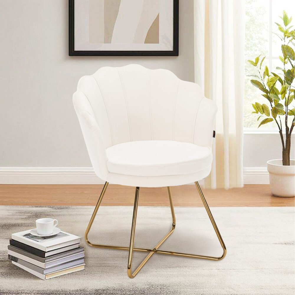 Ein weißer, muschelförmiger Stuhl mit goldenen Beinen steht auf einem Teppich. Ein Stapel Bücher, eine Tasse und eine Pflanze sind zu sehen.