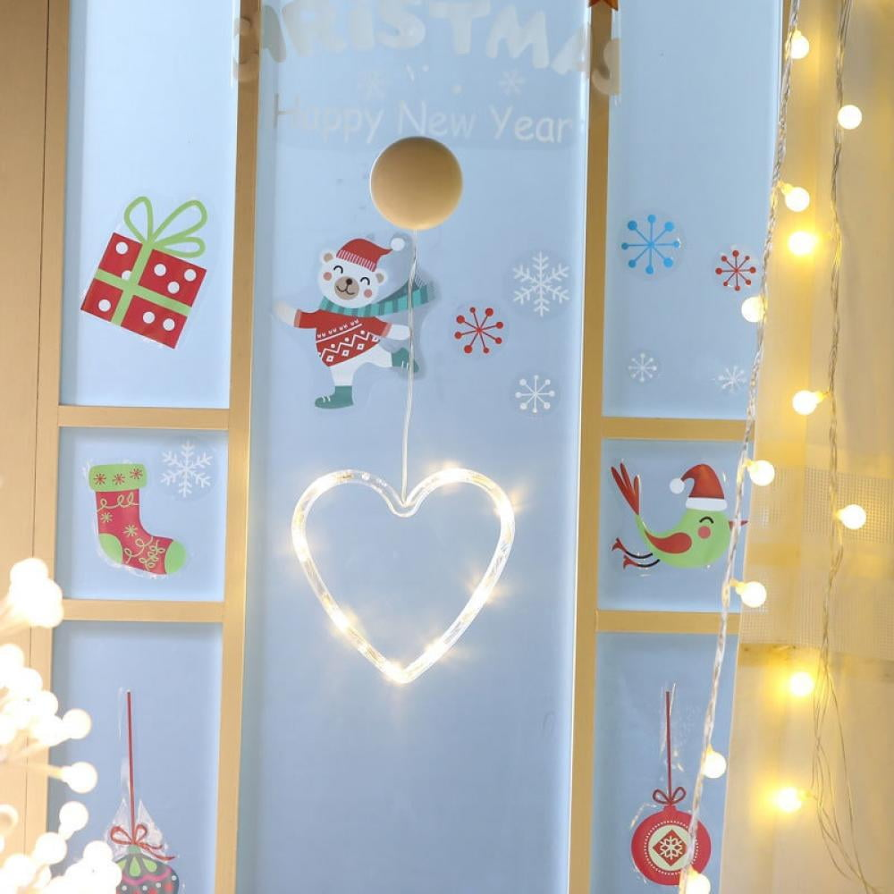 Ein Fenster, dekoriert mit Weihnachtsaufklebern und einem leuchtenden Herzen. Zu den Dekorationen gehören ein Bär, ein Vogel, Schneeflocken und eine Geschenkbox.