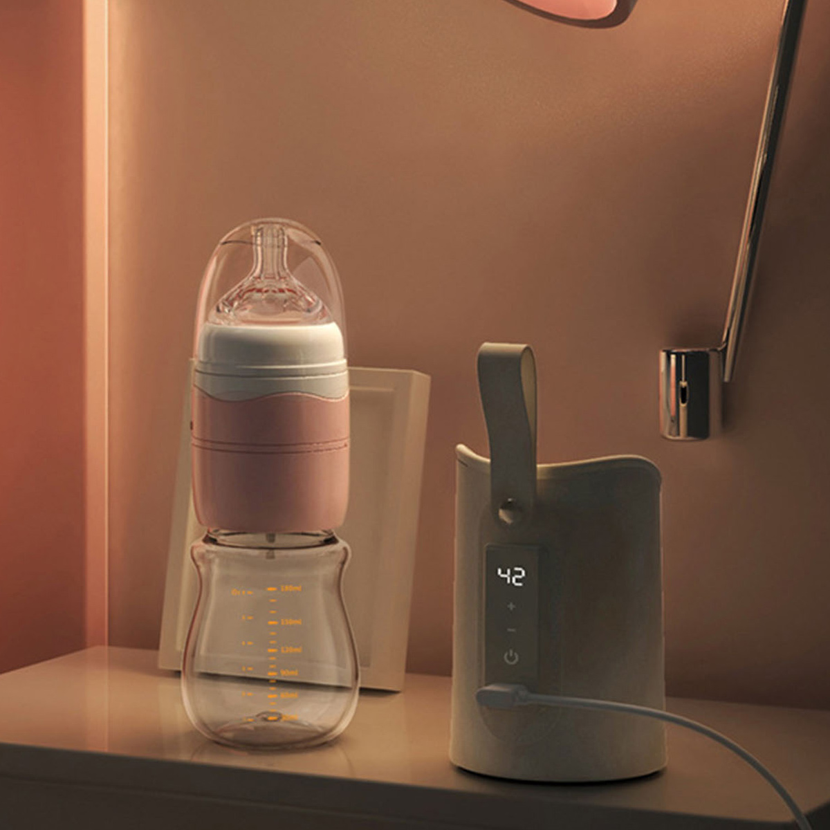 Eine Babyflasche mit rosafarbenem Mittelteil und klarer Basis steht neben einem Wärmegerät. Der Hintergrund ist eine warmtonige Wand.