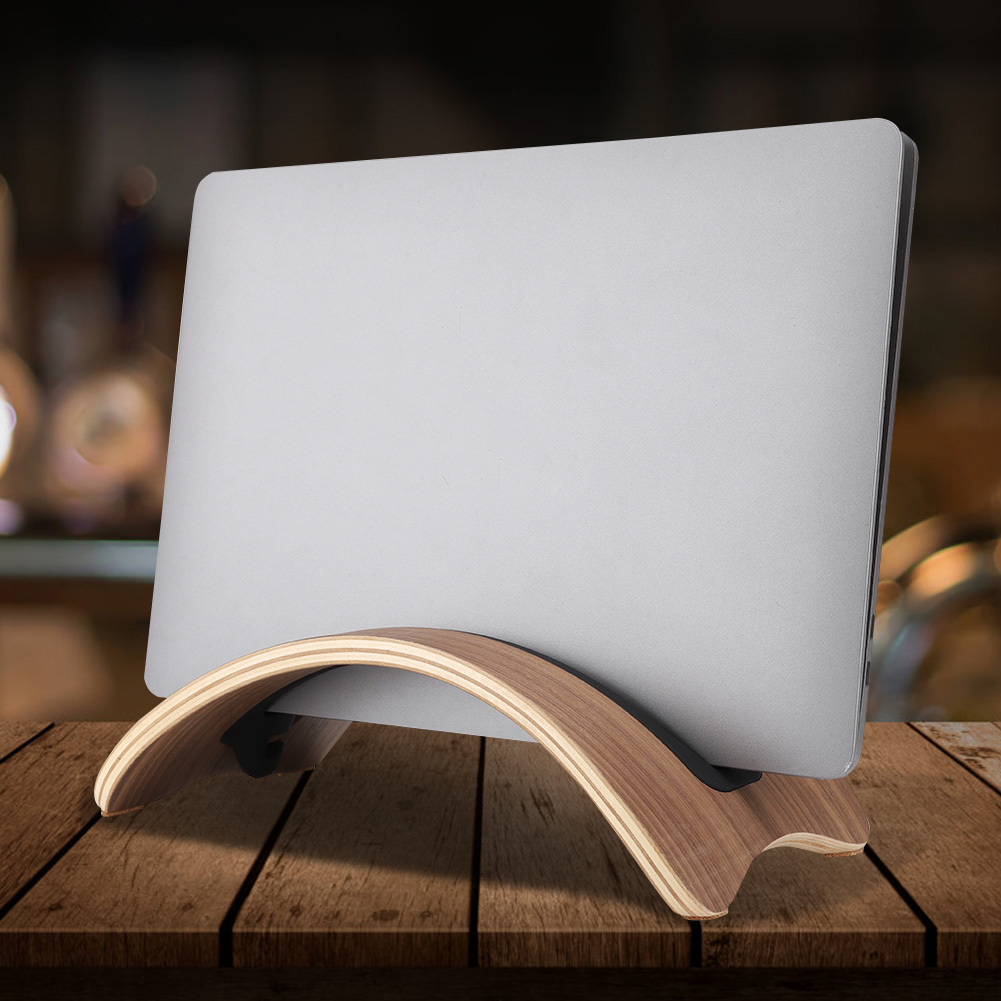 Ein silberner Laptop steht auf einem gebogenen Holzständer. Der Ständer steht auf einem Holztisch. Der Hintergrund ist unscharf mit warmen Tönen.