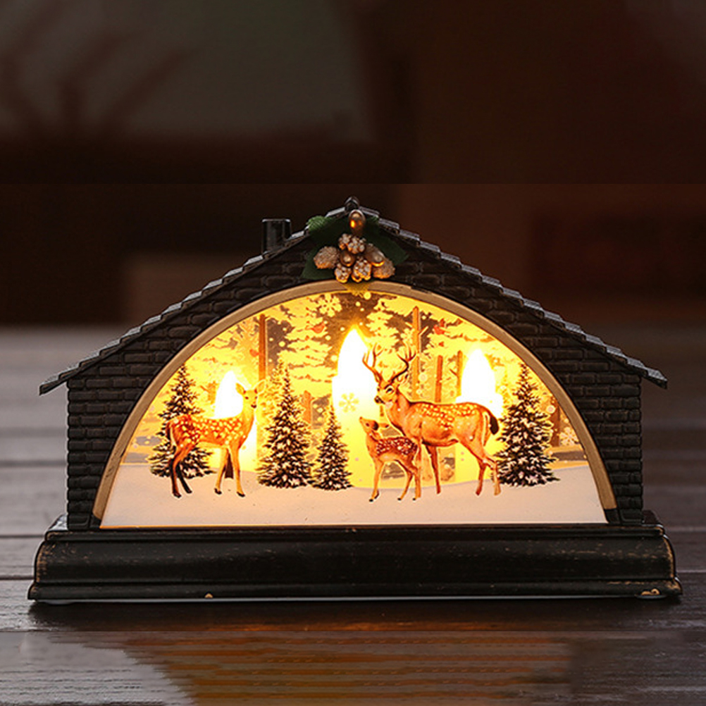 Ein dekoratives, hausförmiges Licht mit Hirschen, Bäumen und Schnee. Es ist von innen beleuchtet und erzeugt eine warme, festliche Weihnachtsszene.