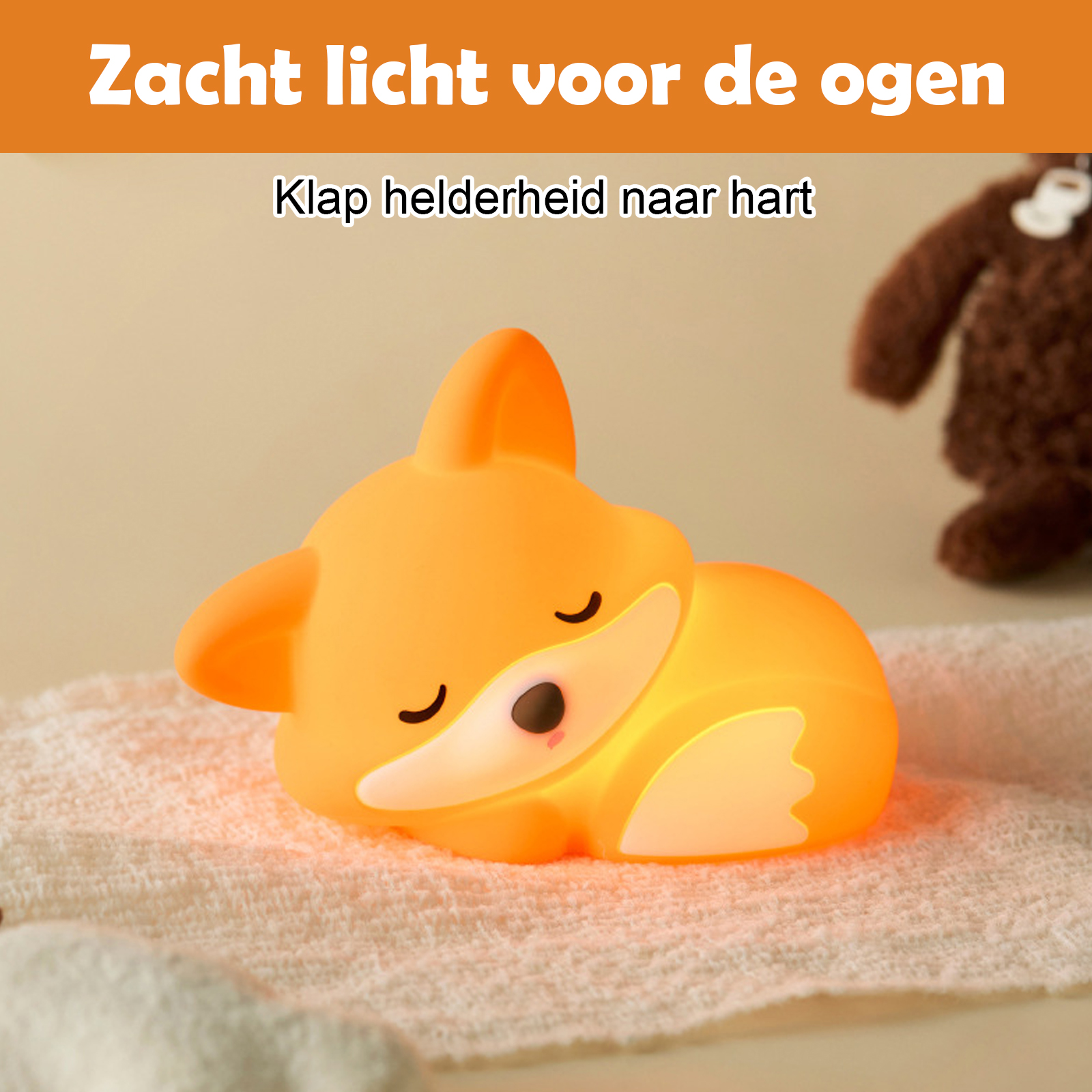 Ein orangefarbenes Fuchsnachtlicht auf einem weißen Handtuch. Brauner Teddybär im Hintergrund. Niederländischer Text oben.
