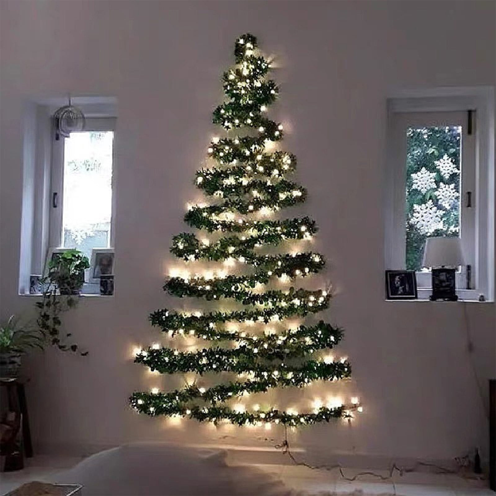 Eine Wand-Weihnachtsbaum aus Girlanden und Lichtern. Fenster auf beiden Seiten. Schneeflocken-Dekorationen sind sichtbar.