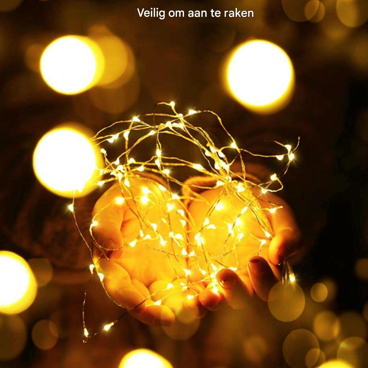 Hände halten eine Lichterkette mit warmweißen Lichtern. Der Hintergrund ist mit großen Bokeh-Lichtern verschwommen. Niederländischer Text: Sicher zu berühren.