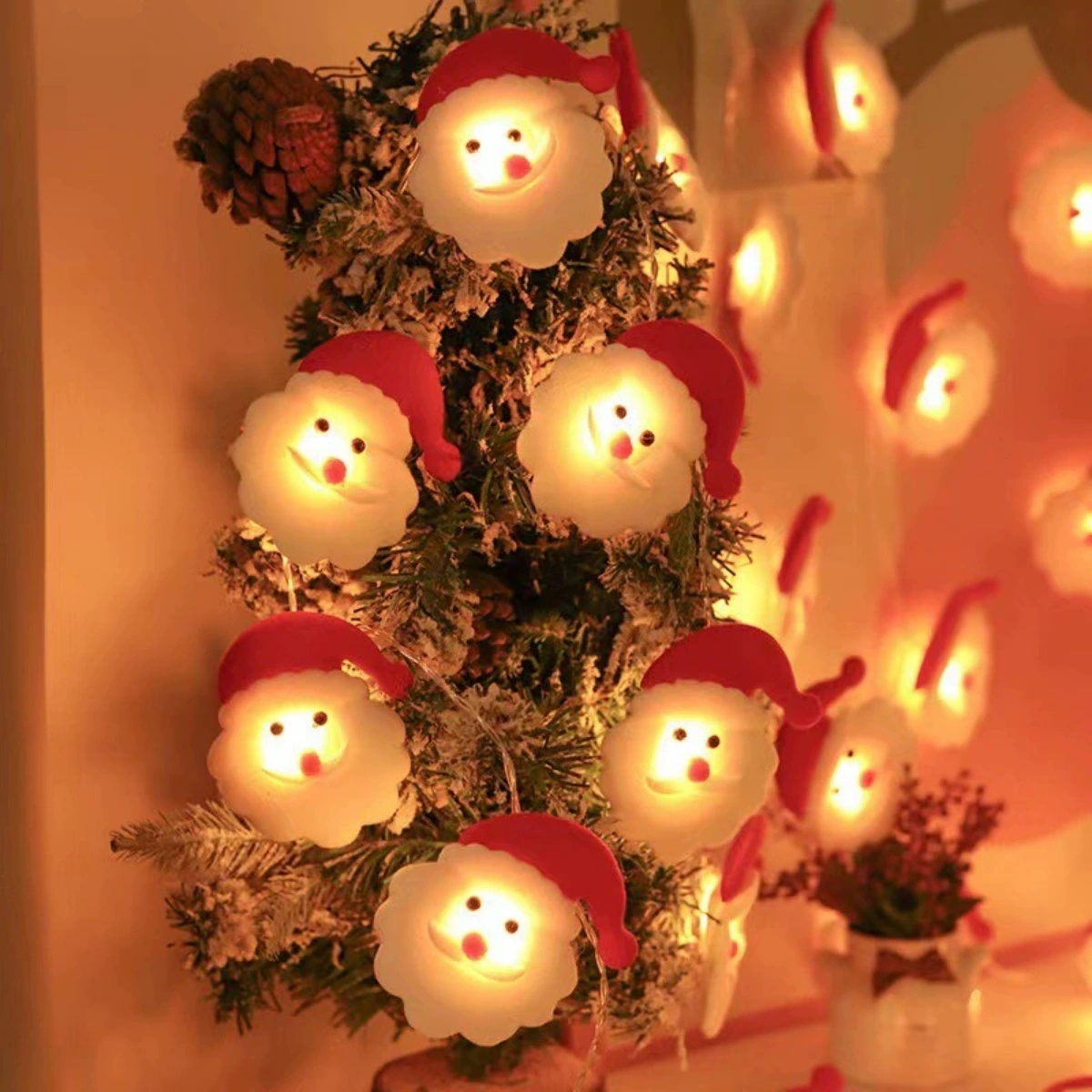 Ein Weihnachtsbaum, geschmückt mit Weihnachtsmann-förmigen Lichtern. Im Hintergrund befinden sich weitere Lichter und ein kleiner Topf mit Pflanzen.