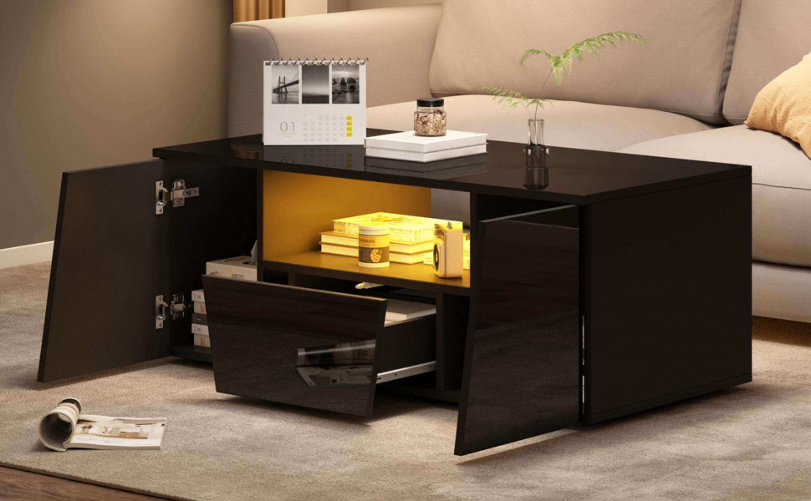 Ein schwarzer Couchtisch mit offenen Türen, Kalender, Büchern und einer Vase mit Pflanze. Sofa im Hintergrund.